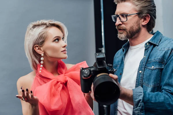 Handsome art director holding digital camera and looking at attractive model — Stock Photo