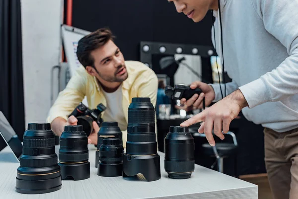 Cropped view of art director pointing with finger at camera lens near photographer — Stock Photo