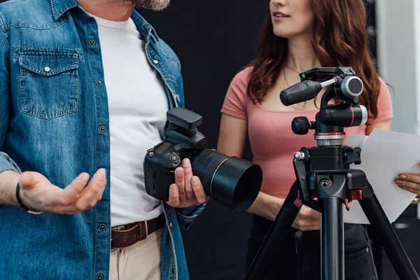 Vista recortada del director creativo de pie con el fotógrafo cerca del trípode - foto de stock