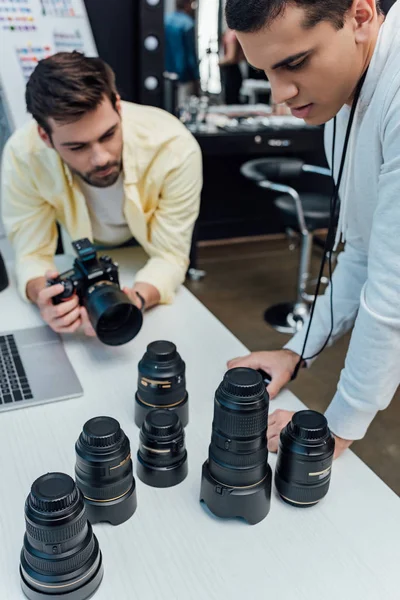Selective focus of handsome art director standing near photographer and looking at photo lenses — Stock Photo