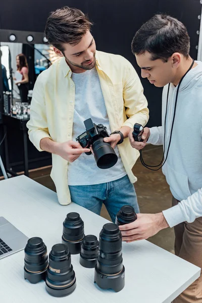 Apuesto director de arte de pie cerca de fotógrafo y sosteniendo lente de foto - foto de stock