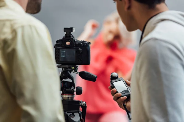 Cropped view of man holding light meter near photographer and digital camera on tripod — Stock Photo