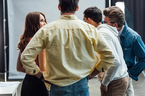 Back view of man standing with hands on hips near coworkers in photo studio — Stock Photo