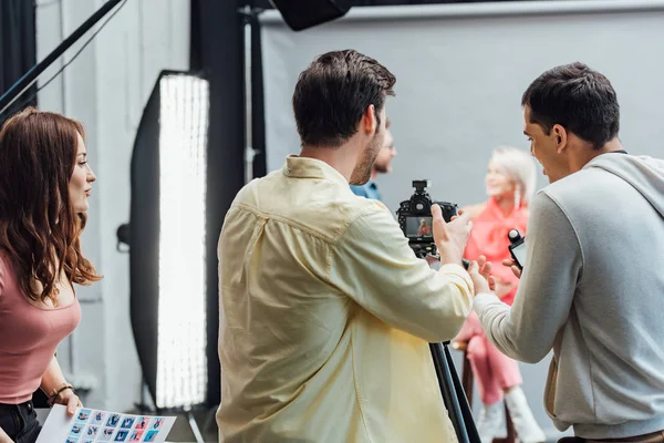 Back view of photographer taking photo near coworkers in photo studio — Stock Photo