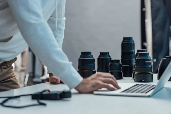 Cropped view of art director using laptop near photo lenses on desk — Stock Photo