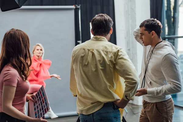 Vue arrière du directeur artistique debout avec la main sur la hanche près des collègues et le modèle dans le studio de photo — Photo de stock