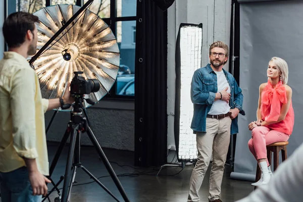 Selektiver Fokus des gut aussehenden Art Directors, der mit der Hand in der Tasche in der Nähe eines attraktiven Modells steht und den Fotografen ansieht — Stockfoto