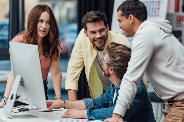 Handsome art director in glasses looking at happy assistants — Stock Photo