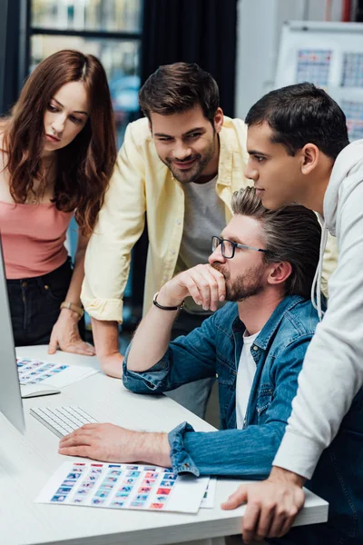 Happy man looking at art director near coworkers — Stock Photo