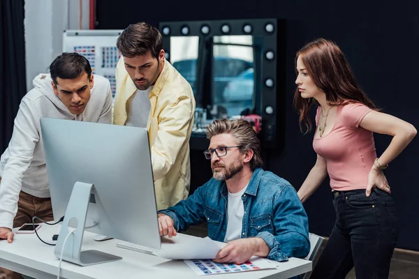 Diretor criativo em óculos olhando para monitor de computador com colegas de trabalho — Fotografia de Stock