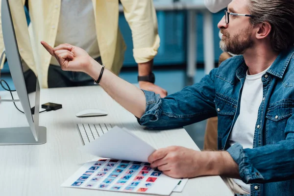 Vue recadrée de l'assistant debout près du directeur artistique pointant du doigt le moniteur de l'ordinateur — Photo de stock