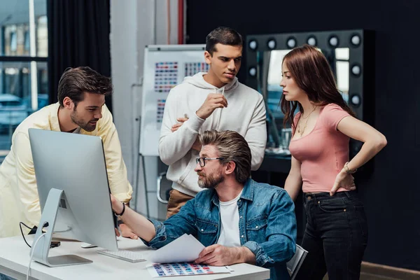 Diretor criativo em óculos olhando assistente perto de monitor de computador — Fotografia de Stock