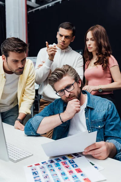 Selective focus of pensive art director looking at papers near assistants — Stock Photo