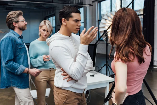 Enfoque selectivo del gesto del hombre cerca del director de arte y compañeros de trabajo en el estudio de fotografía - foto de stock