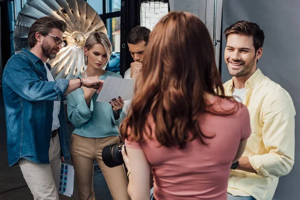 Back view of photographer standing near happy man and coworkers in photo studio — Stock Photo