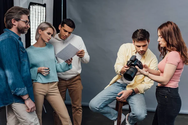 Fotógrafo sosteniendo cámara digital cerca modelo guapo y compañeros de trabajo - foto de stock