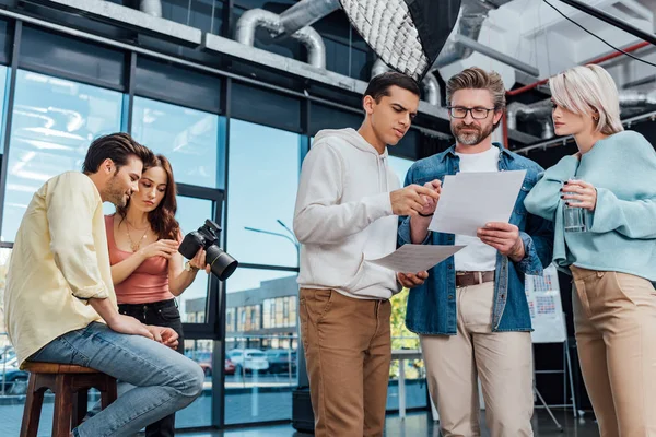 Diretor criativo em óculos olhando para foto perto de colegas de trabalho — Fotografia de Stock