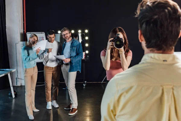 Enfoque selectivo de fotógrafo tomando fotos de hombre cerca de director de arte y compañeros de trabajo - foto de stock