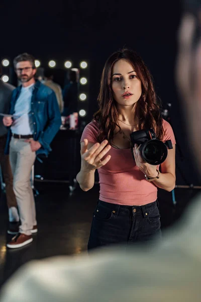 Messa a fuoco selettiva di attraente fotografo parlando mentre gesticolando e guardando l'uomo in studio fotografico — Foto stock