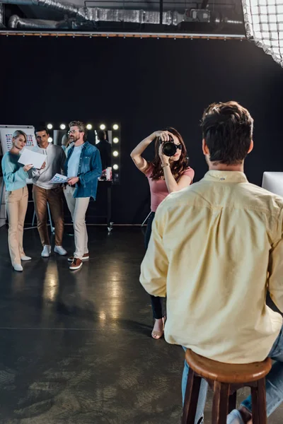 Selective focus of photographer taking photo of man sitting on chair in photo studio — Stock Photo