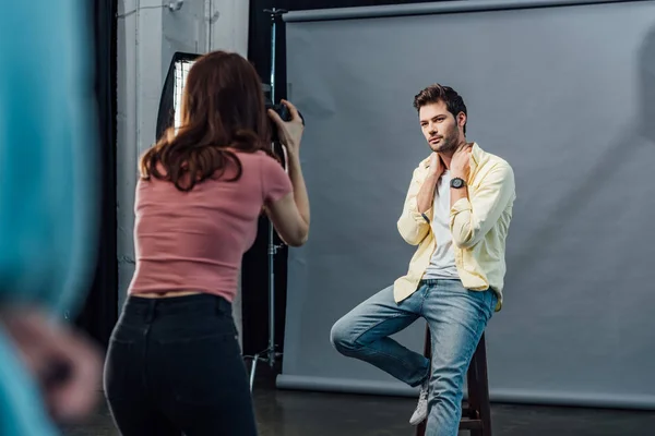 Rückansicht des Fotografen, der ein Foto des hübschen Models macht, das auf einem Stuhl posiert — Stockfoto