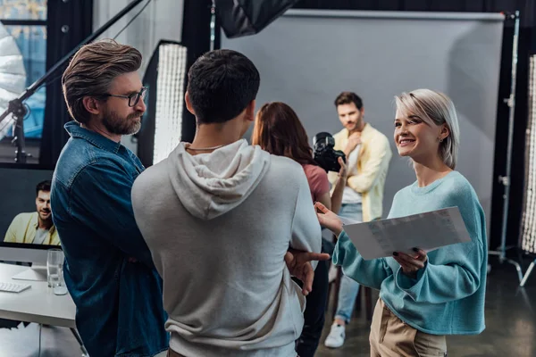 Enfoque selectivo de la mujer feliz mirando compañero de trabajo cerca de director de arte en el estudio de fotos - foto de stock