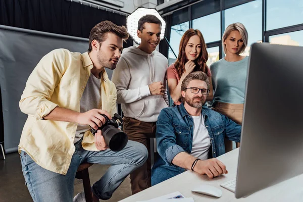 Selective focus of happy creative director and assistants looking at computer monitor in photo studio — Stock Photo