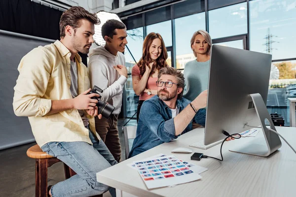 Selective focus of creative director looking at happy assistants in photo studio — Stock Photo