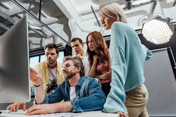 Low angle view of creative director and assistants looking at computer monitor in photo studio — Stock Photo