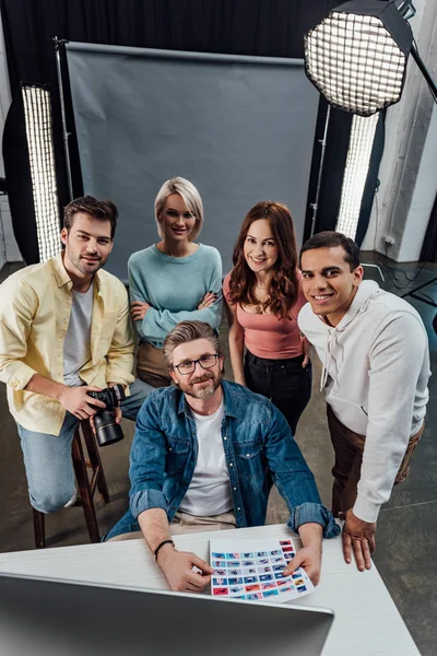 Overhead view of cheerful creative director and assistants looking at camera in photo studio — Stock Photo