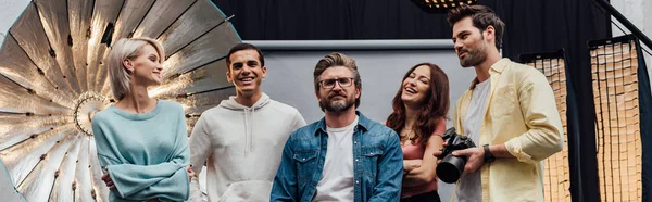 Panoramic shot of coworkers smiling while looking at camera in photo studio — Stock Photo