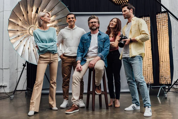 Tiro panorámico del equipo feliz sonriendo mientras mira a la cámara en el estudio de fotos - foto de stock