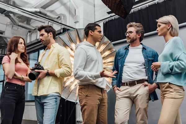 Directeur artistique debout avec les mains dans les poches près des collègues dans le studio de photo — Photo de stock