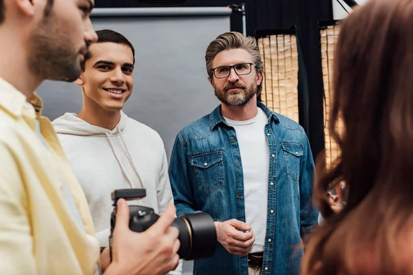 Selective focus of happy man looking at camera near art director and photographer — Stock Photo