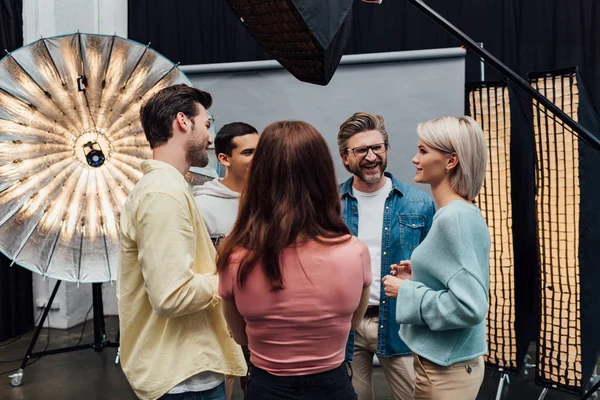 Back view of woman standing near cheerful coworkers in photo studio — Stock Photo