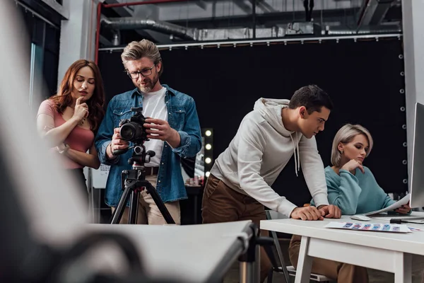 Foco seletivo do diretor de arte que está perto de fotógrafo e colegas de trabalho — Fotografia de Stock