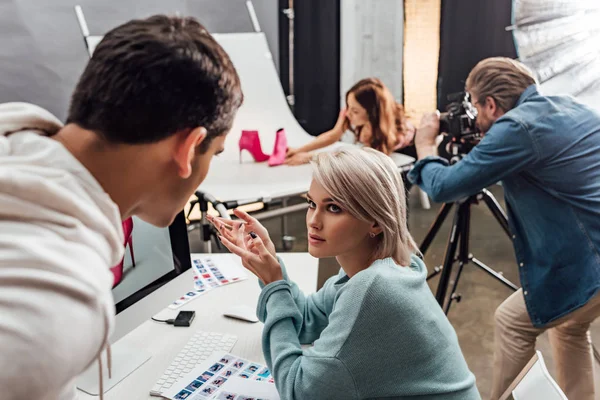 Attraktiver Art Director gestikuliert neben Computermonitor und schaut Assistentin an — Stockfoto