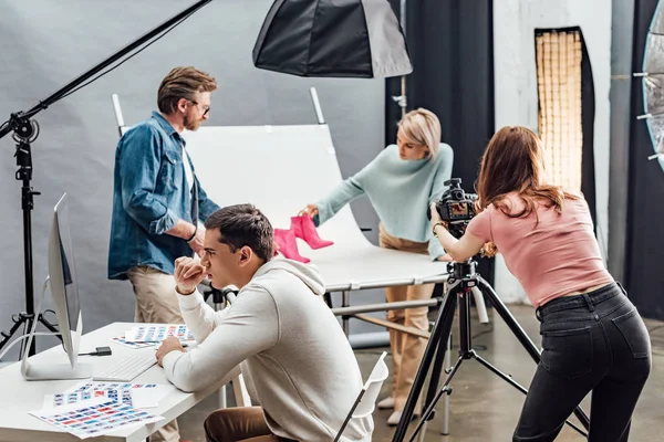 Selektiver Fokus eines gutaussehenden Mannes, der in der Nähe von Kollegen im Fotostudio auf den Computermonitor blickt — Stockfoto