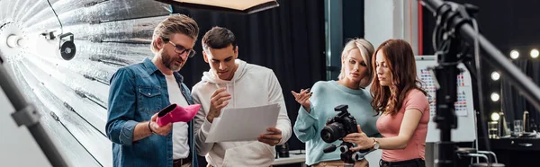 Panoramic shot of art director holding pink shoe near coworkers in photo studio — Stock Photo