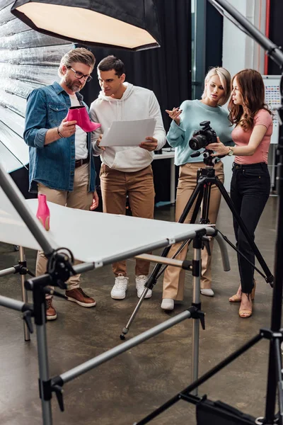 Director de arte sosteniendo zapato rosa cerca asistente en estudio de fotos - foto de stock