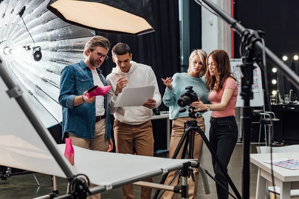 Селективный фокус арт-директора, держащего розовую обувь рядом с коллегами в фотостудии — стоковое фото