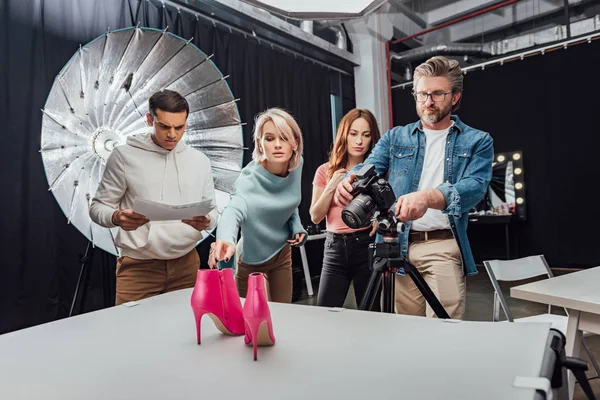 Photographer photo shooting pink shoes near coworkers in photo studio — Stock Photo
