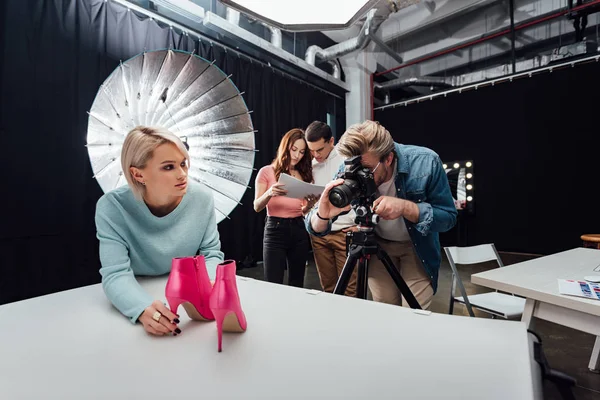 Fotógrafo foto tiro zapatos cerca de compañeros de trabajo en estudio de fotos - foto de stock