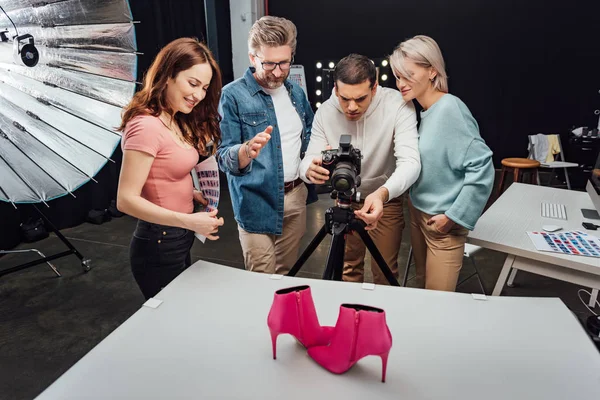 Foto fotógrafo tiro sapatos rosa perto de colegas de trabalho felizes no estúdio de fotografia — Fotografia de Stock