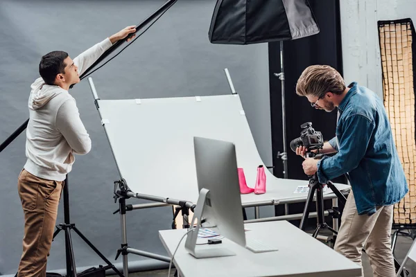 Bonito assistente tocando refletor enquanto fotógrafo foto tiro sapatos — Fotografia de Stock