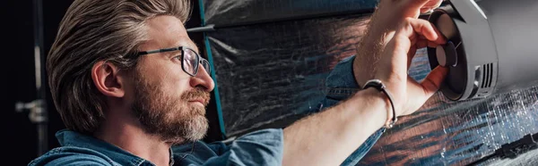 Panoramic shot of bearded art director touching reflector in photo studio — Stock Photo