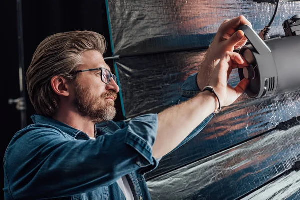 Director de arte barbudo tocando reflector en estudio fotográfico - foto de stock