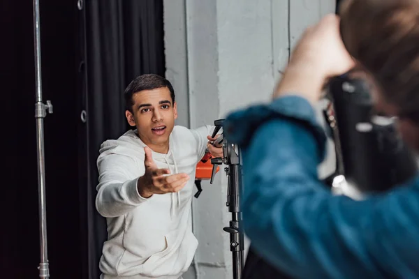 Selective focus of handsome assistant gesturing while talking near man in photo studio — Stock Photo