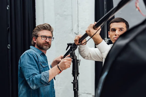 Selektiver Fokus gutaussehender Männer mit Lichtständer im Fotostudio — Stockfoto