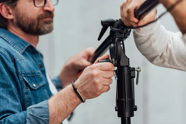 Cropped view of man holding light stand with assistant in photo studio — Stock Photo